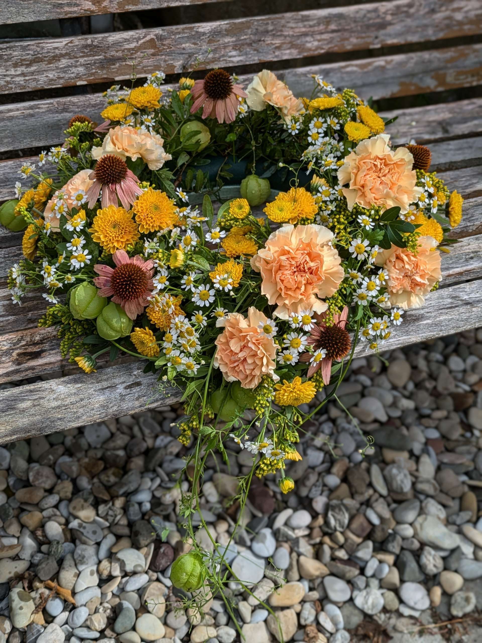 Runder Blumenkranz mit gemischten Blüten auf einer Holzbank