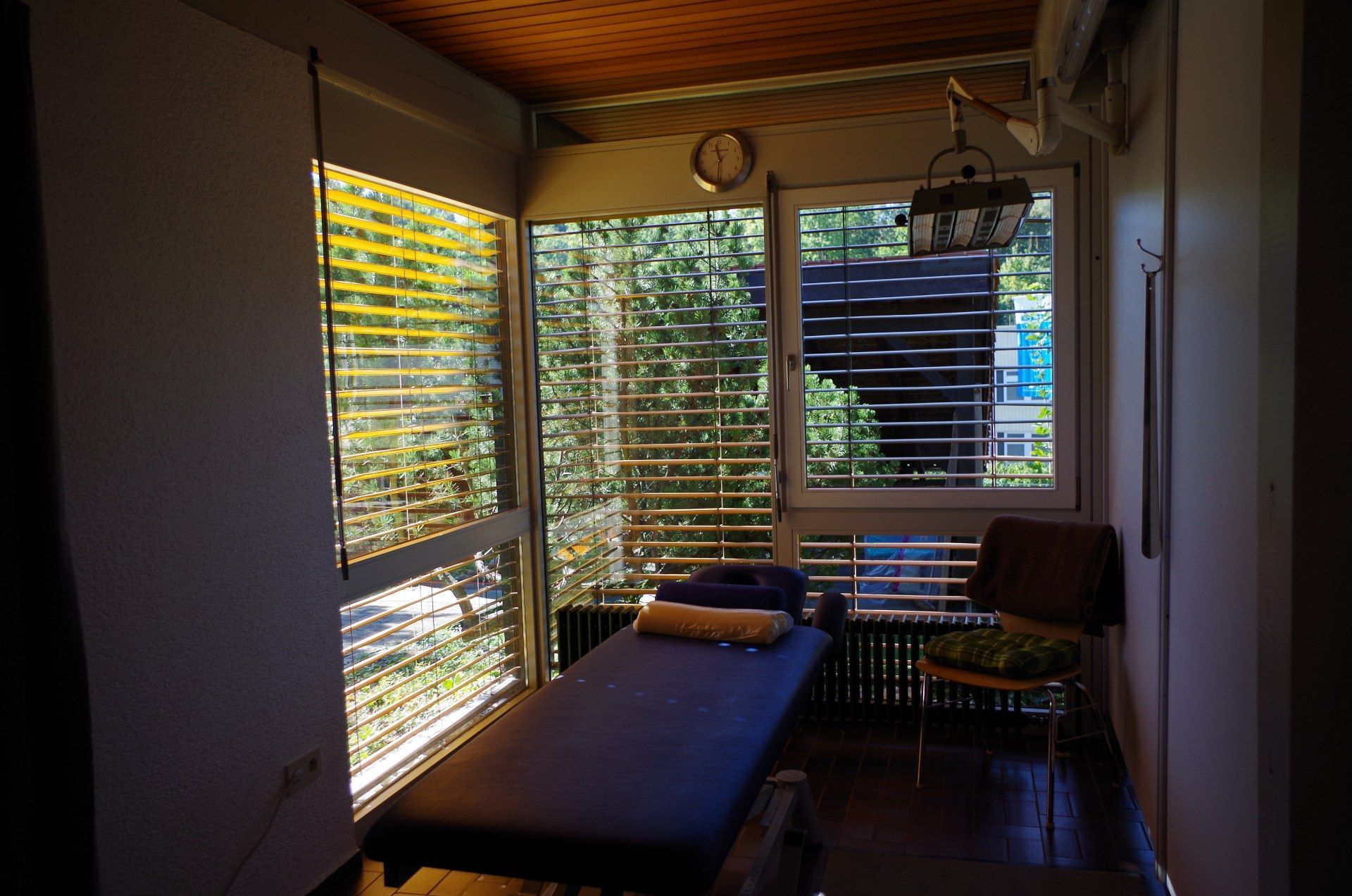 Massagetherapieraum mit Bett, Stuhl und Fenster mit Blick auf Bäume.