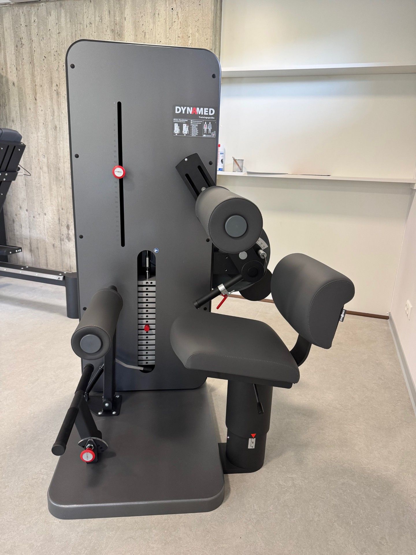 Graues Trainingsgerät mit Armpolstern und Sitz, im Innenbereich.