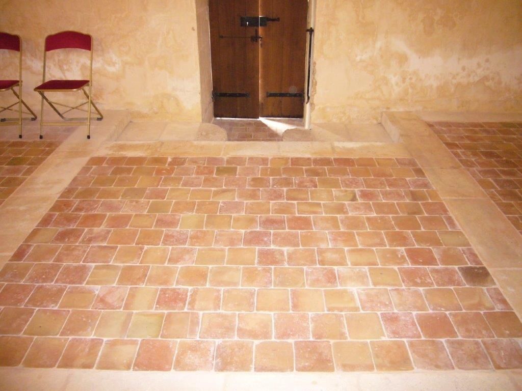 Sol carrelé nu dans une pièce rustique avec une porte en bois et deux chaises rouges contre le mur.