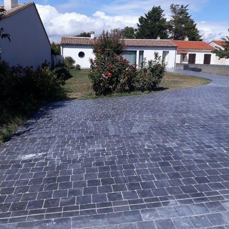 Allée pavée menant à des maisons blanches aux toits rouges et à un arbuste fleuri dans une cour ensoleillée