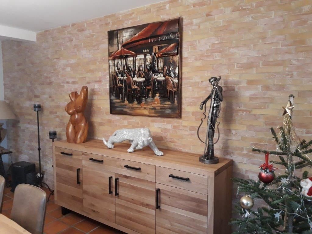 Salon avec mur de briques, buffet en bois, œuvres d'art, sculptures et sapin de Noël décoré