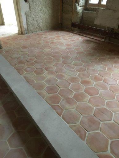 Pièce carrelée vide, avec un sol en carreaux hexagonaux roses et des murs inachevés, éclairée par la lumière du jour provenant d'une fenêtre.