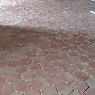 Gros plan sur un sol carrelé hexagonal rouge avec une tache de soleil et d'ombre.