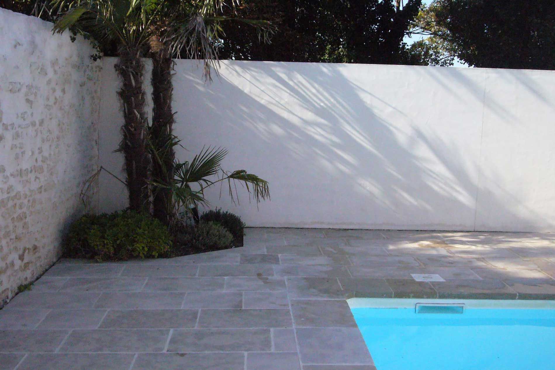 Terrasse carrelée vide à côté d'une piscine turquoise et d'un mur blanc avec un palmier dans un coin