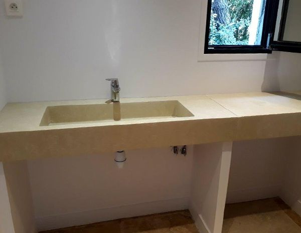 Comptoir de lavabo blanc avec robinet et fenêtre au-dessus, adossé à un mur uni.