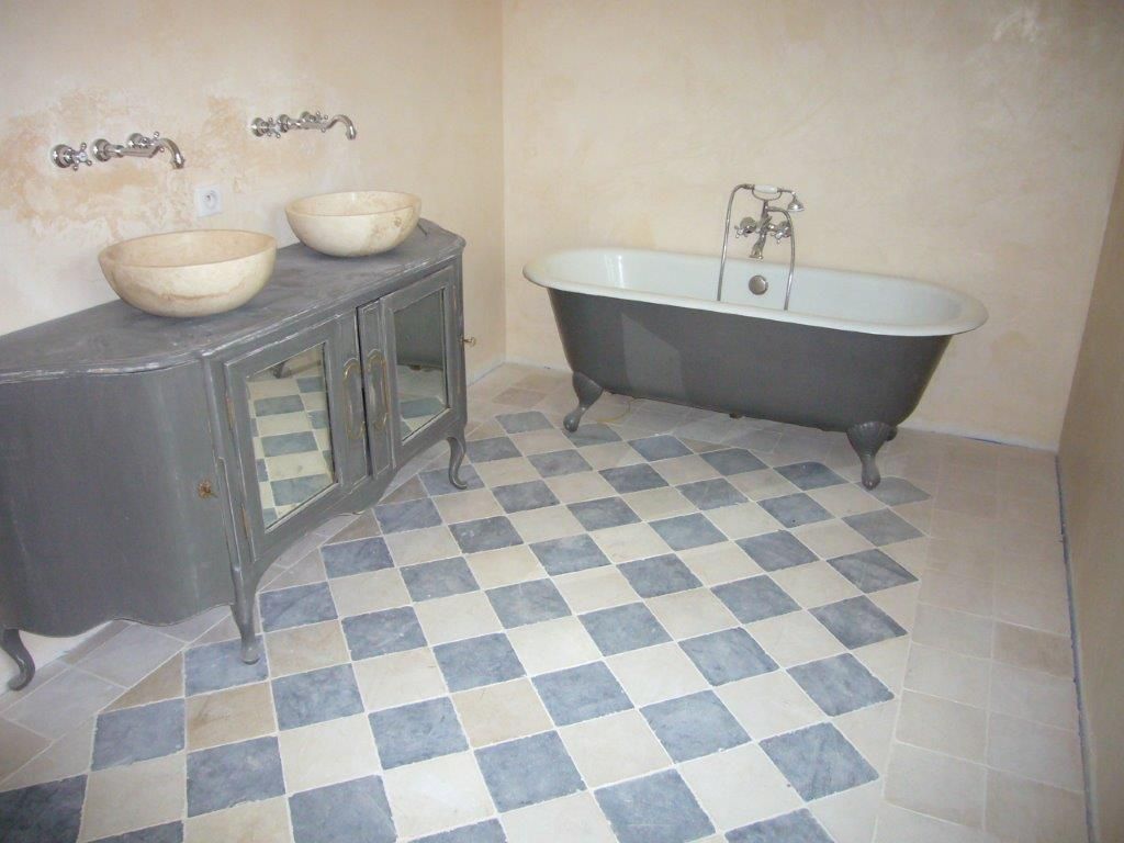 Petite salle de bains avec baignoire sur pieds, double vasque et sol en carrelage à damier bleu et blanc.
