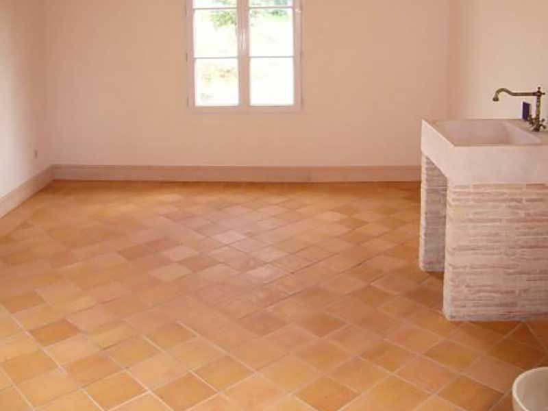 Pièce vide avec sol en terre cuite, fenêtre et lavabo blanc contre un mur couleur pêche