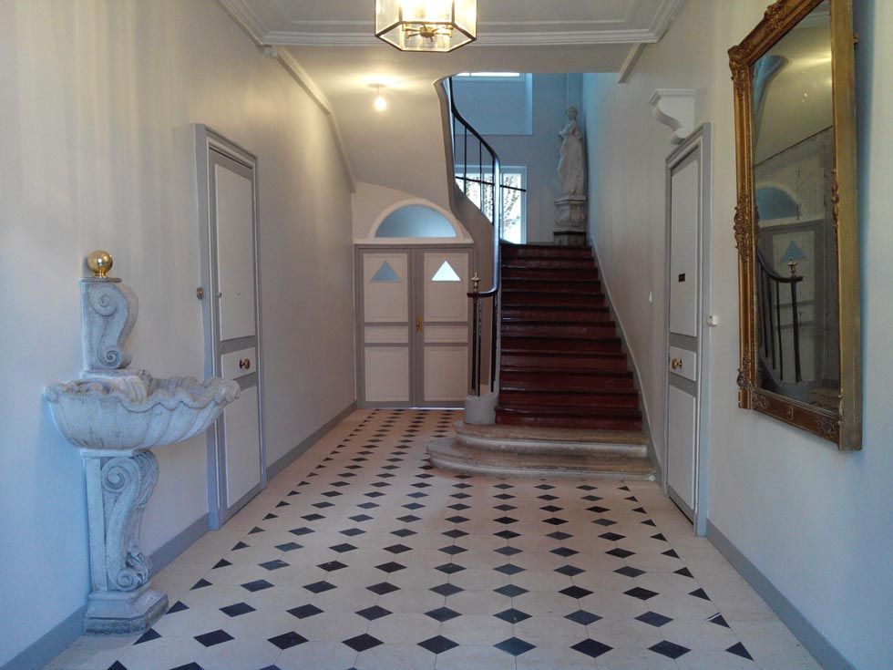 Élégant couloir avec sol en carrelage à damier, escalier, miroir mural et sculpture décorative de fontaine