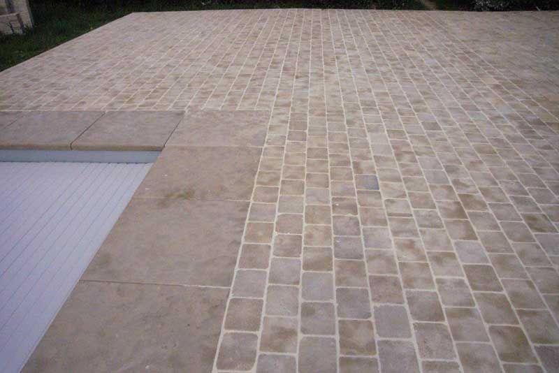 Terrasse pavée en pierre à côté d'une piscine, avec une bordure en béton beige et une allée carrelée.