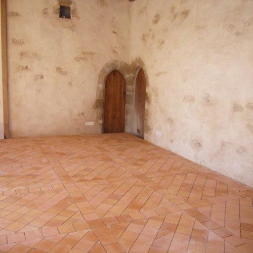 Pièce vide avec un sol carrelé beige à motifs, des murs blancs défraîchis et deux portes étroites en bois dans un coin.