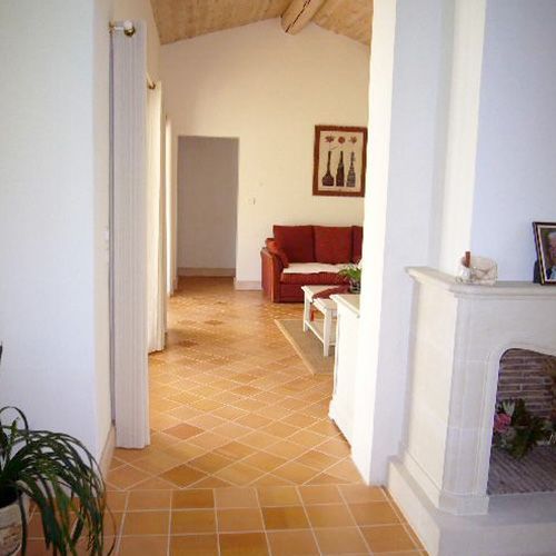 Hall d'entrée lumineux avec sol en carrelage de terre cuite, murs blancs, canapé rouge et cheminée.