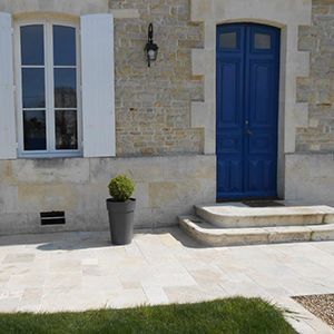 Porte bleue et fenêtre à encadrement blanc sur la façade en pierre d'une maison avec marches et plante en pot.