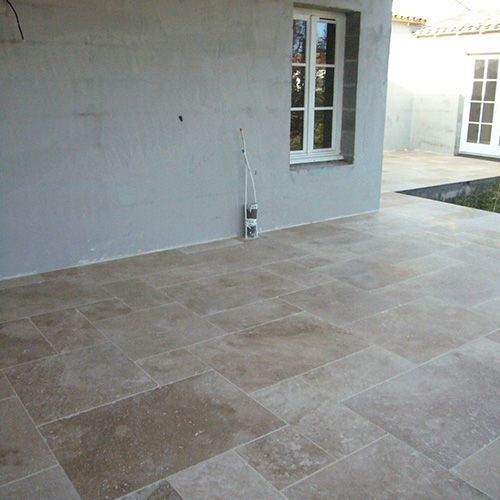 Patio couvert avec sol en dalles de pierre beige, murs en stuc gris et porte vitrée
