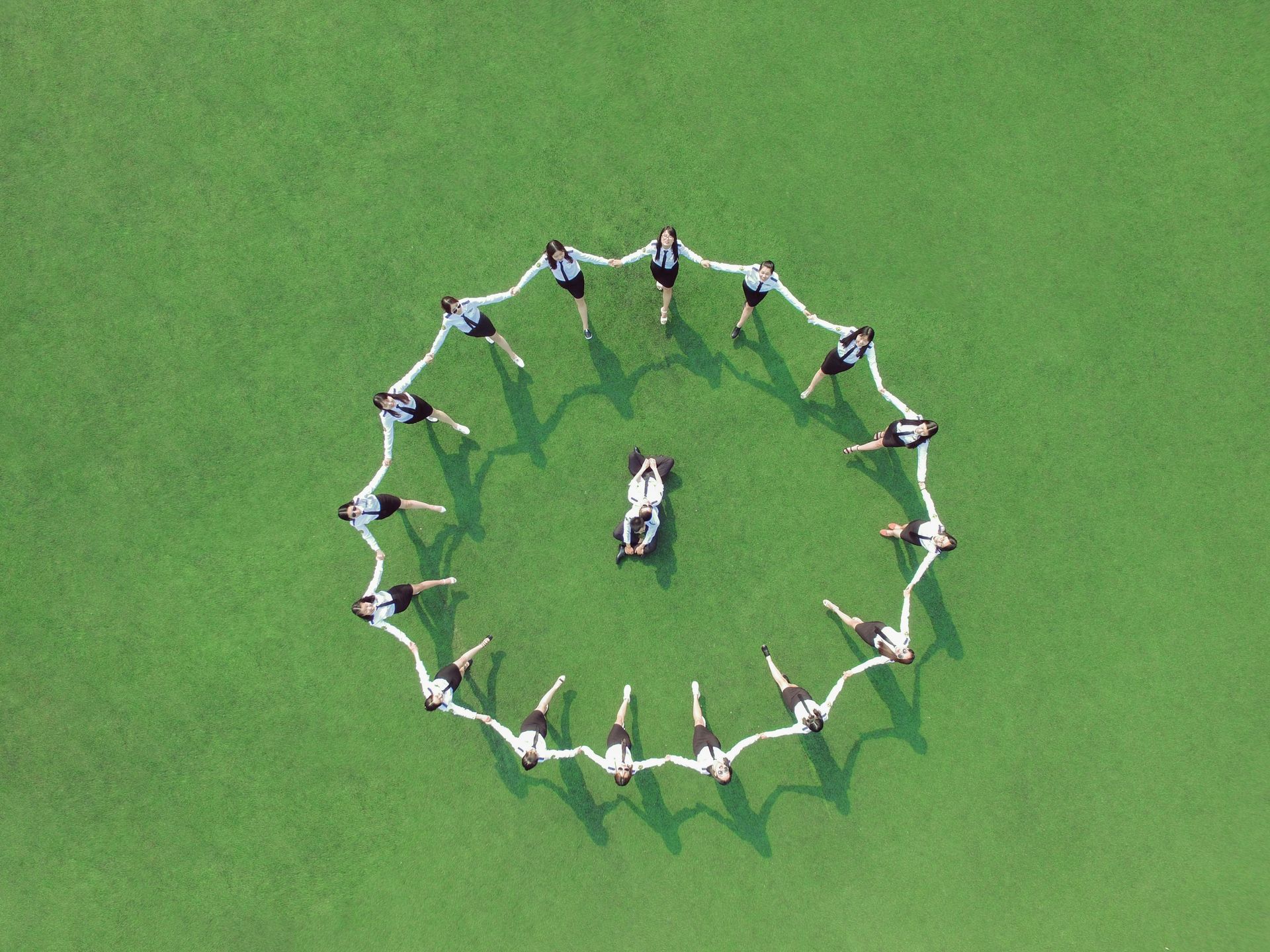 Eine Gruppe von Menschen steht in einem Kreis auf einer grünen Wiese.