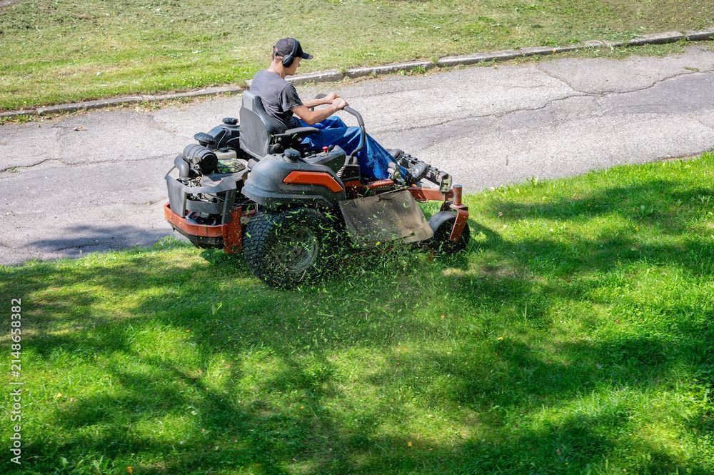 Person auf einem roten Rasenmäher an einem Grashang neben einem gepflasterten Weg