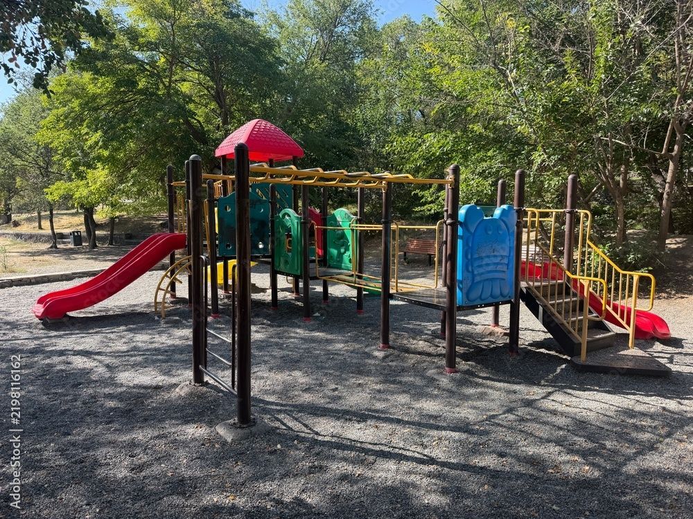 Outdoor-Spielplatz mit roten Rutschen, grünen Tunneln und Klettergerüsten unter Bäumen