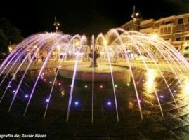 Una fuente se ilumina por la noche con luces violetas.