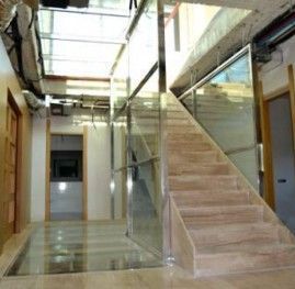 Un pasillo con escaleras y barandilla de cristal.