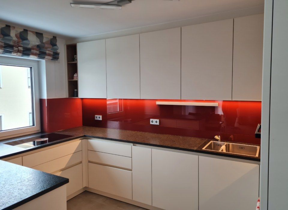 Moderne weiße Küche mit roter Küchenrückwand und Granitarbeitsplatten.