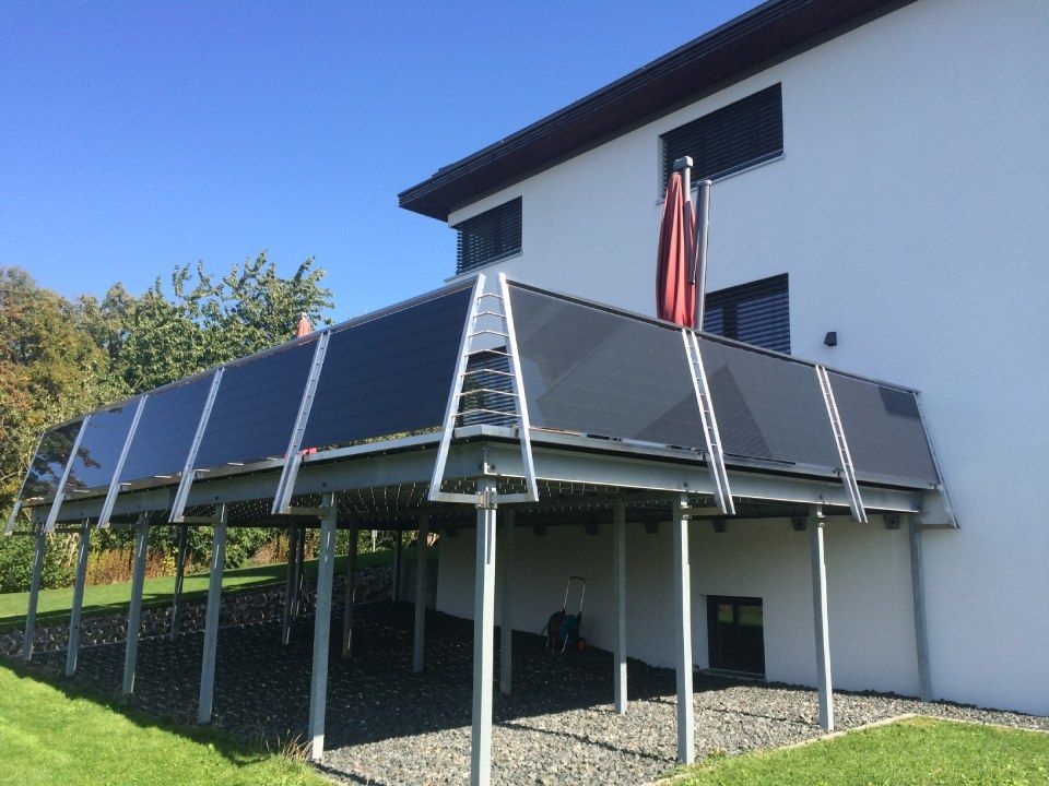 Terrasse mit schwarzen Solarmodulen und einem roten Sonnenschirm auf einem weißen Haus.