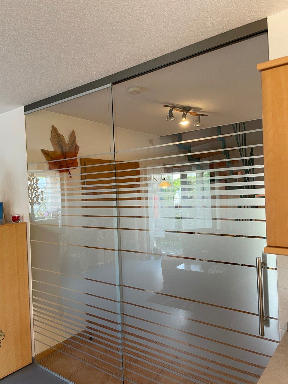 Glasschiebetür mit horizontalen Milchstreifen. Innenansicht, Holzschränke auf jeder Seite.