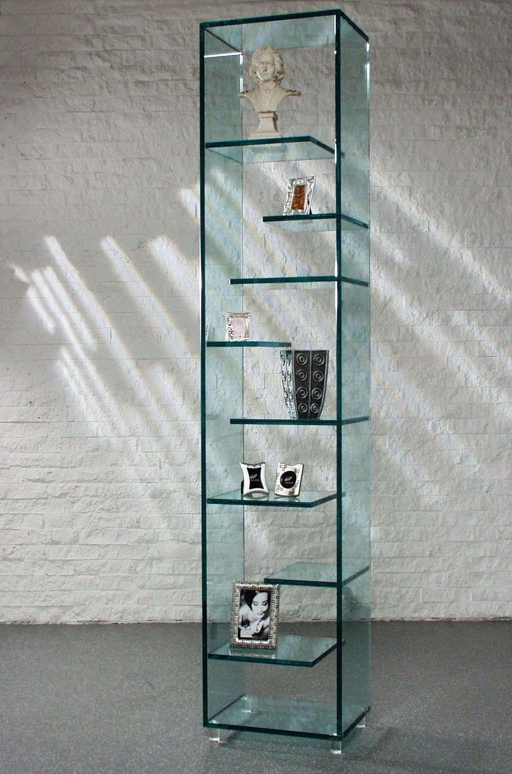 Glasvitrine mit sechs Regalen für Dekorationsgegenstände vor einer Ziegelwand.