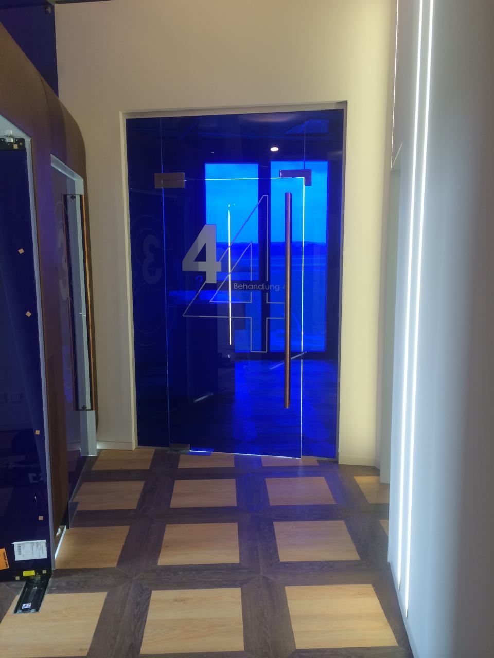 Blaue Glastür mit der Nummer 4, Edelstahlgriffe, in einem modernen Flur mit Holz und Beleuchtungskörpern.