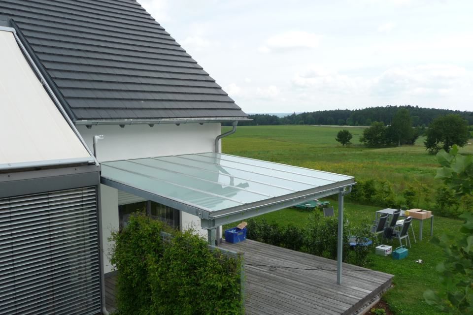 Eine überdachte Terrasse an einem Haus mit einer grünen Wiese im Hintergrund.