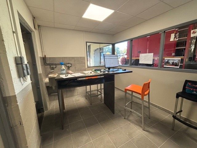 Espace de bureau : bureau avec ordinateur, tabouret orange, fenêtre donnant sur l’extérieur, armoires rouges.