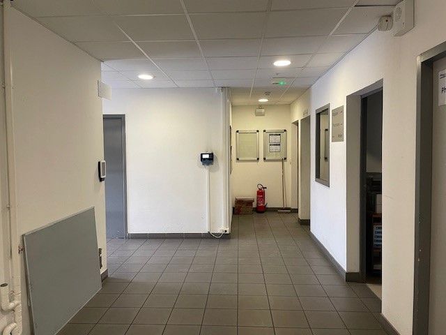 Couloir avec sol carrelé gris, murs blancs, portes et extincteur.