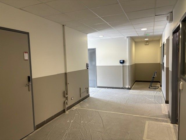 Couloir avec murs bicolores (beige et crème), portes des deux côtés et revêtement de protection au sol.