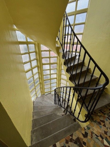 Un escalier en colimaçon avec une rampe noire, de grandes fenêtres et des murs jaunes.