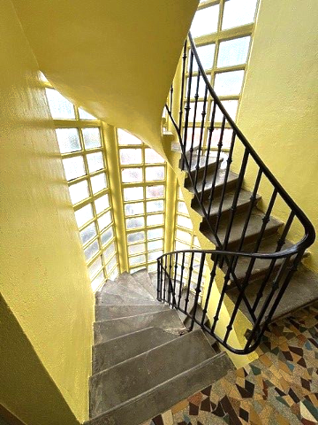 Escalier en colimaçon jaune avec rampe noire et nombreuses fenêtres.