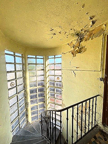Escalier en colimaçon avec fenêtres en pavés de verre et peinture jaune écaillée.