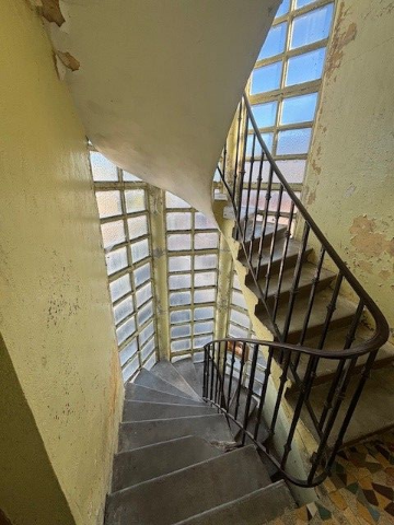 Escalier en colimaçon avec rampe métallique et mur vitré. Murs jaunis par le temps et marches usées.