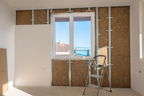 Mur intérieur en construction avec fenêtre ; montants métalliques, isolation et plaques de plâtre visibles.