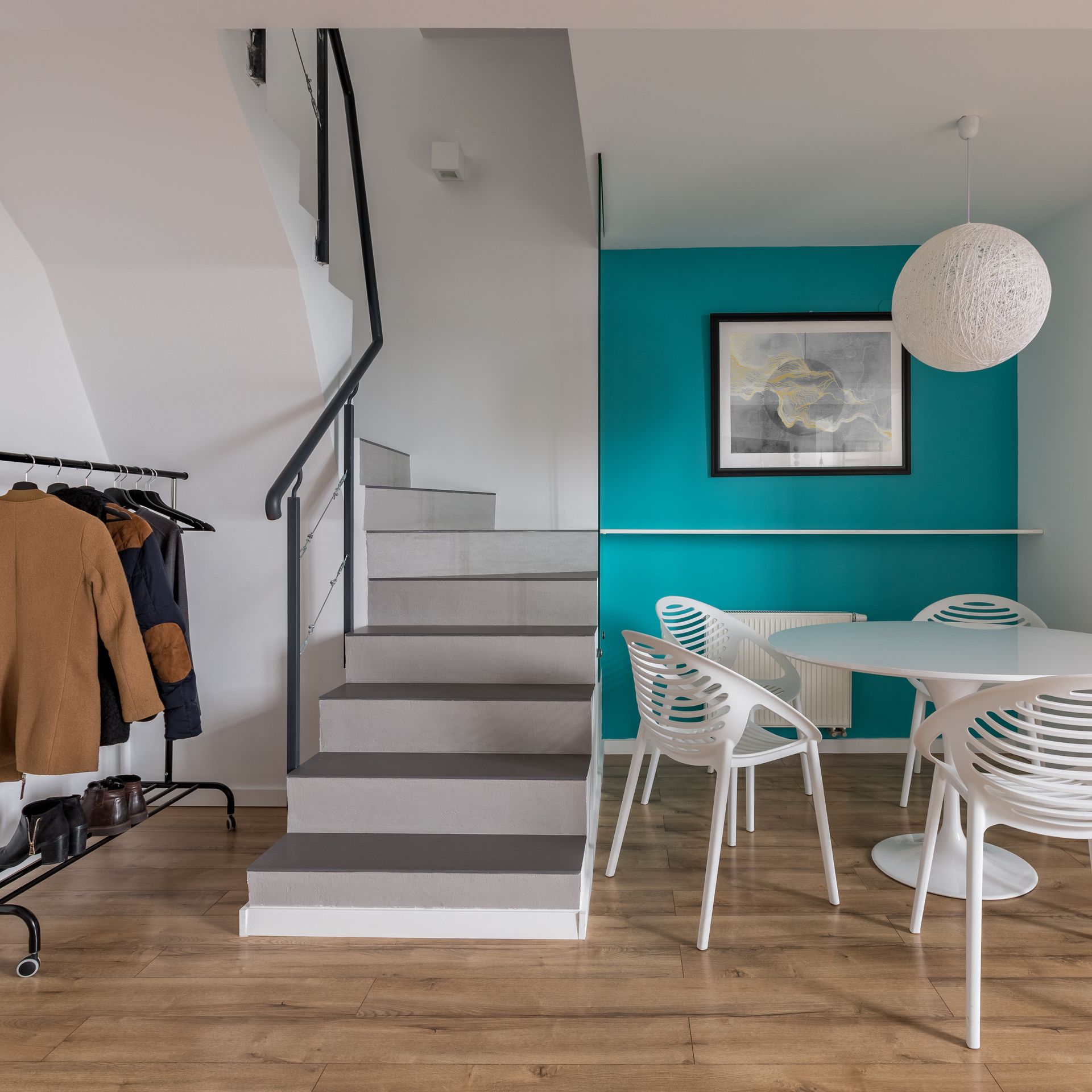 Un petit coin repas avec une table ronde et des chaises blanches, à côté d'un mur turquoise.