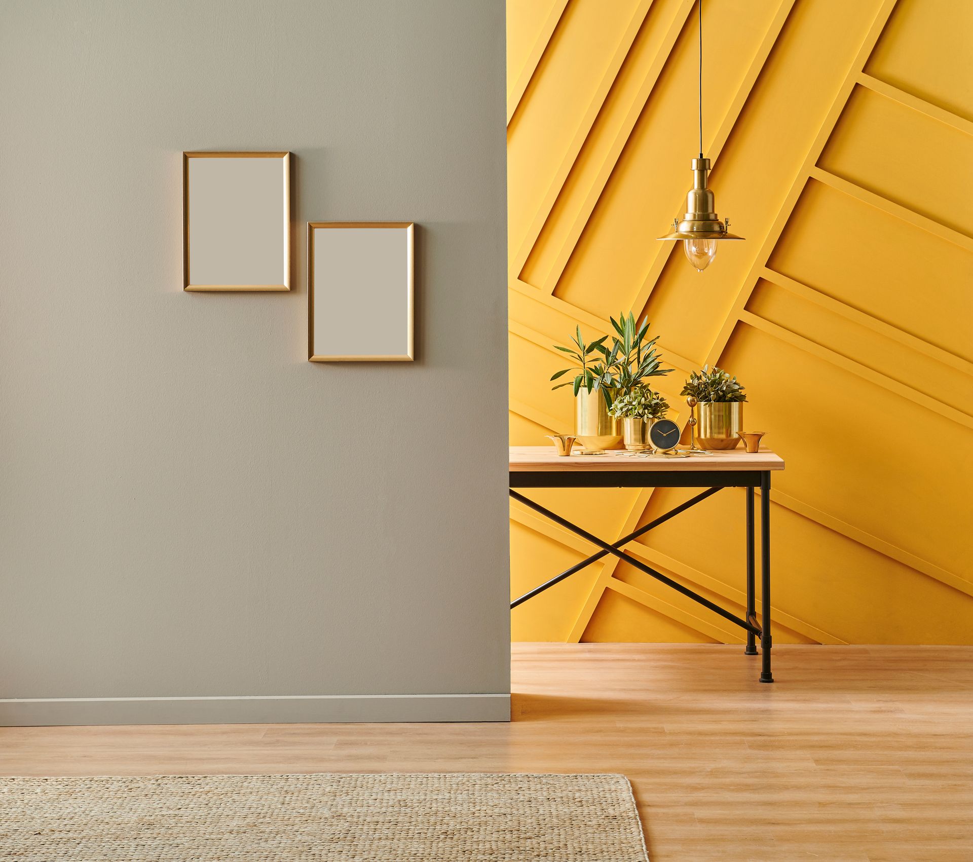 Pièce aux murs gris et jaunes, une table avec des plantes, des cadres dorés, une suspension lumineuse et un tapis.