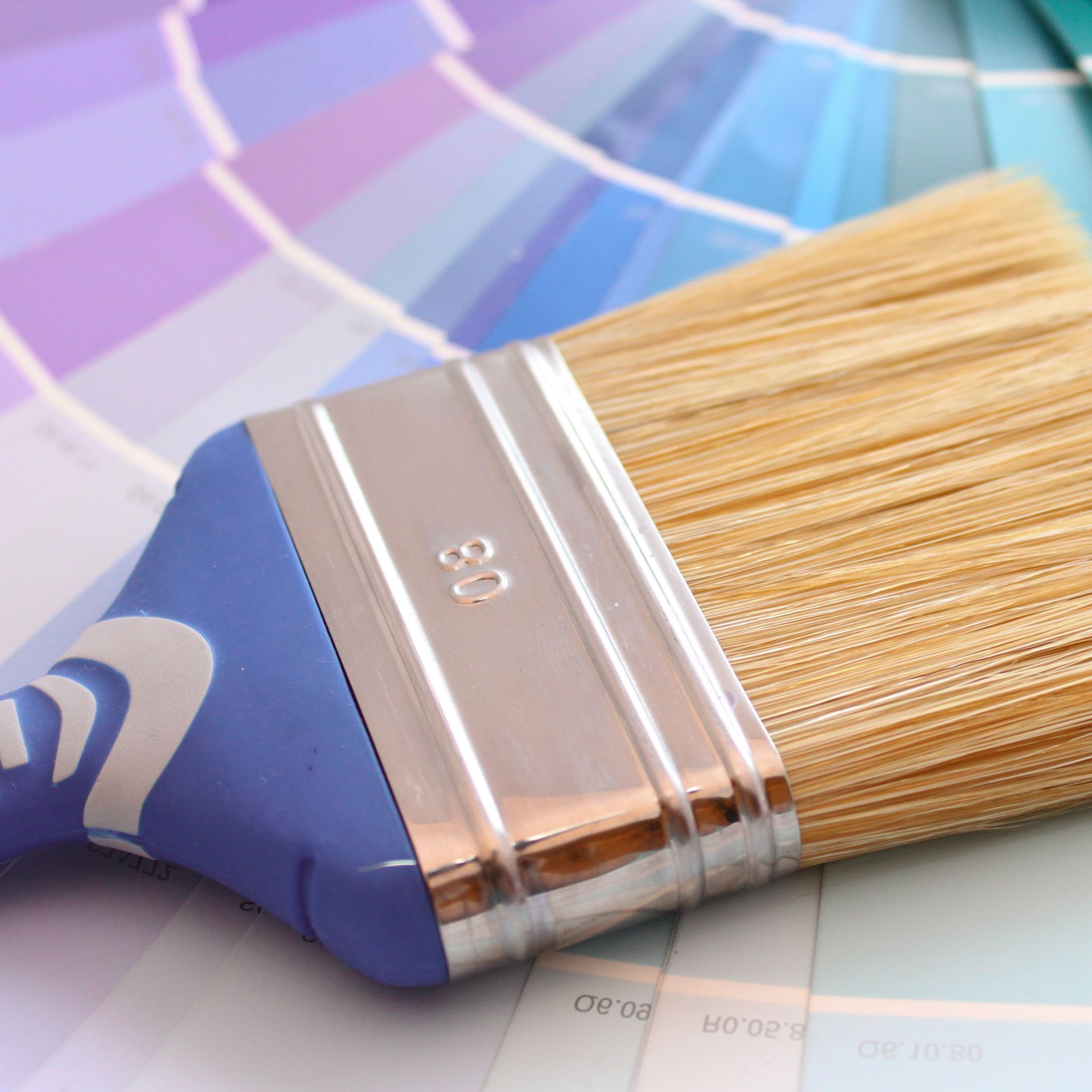 Un pinceau posé sur une palette de couleurs composée d'échantillons bleus, violets et verts.