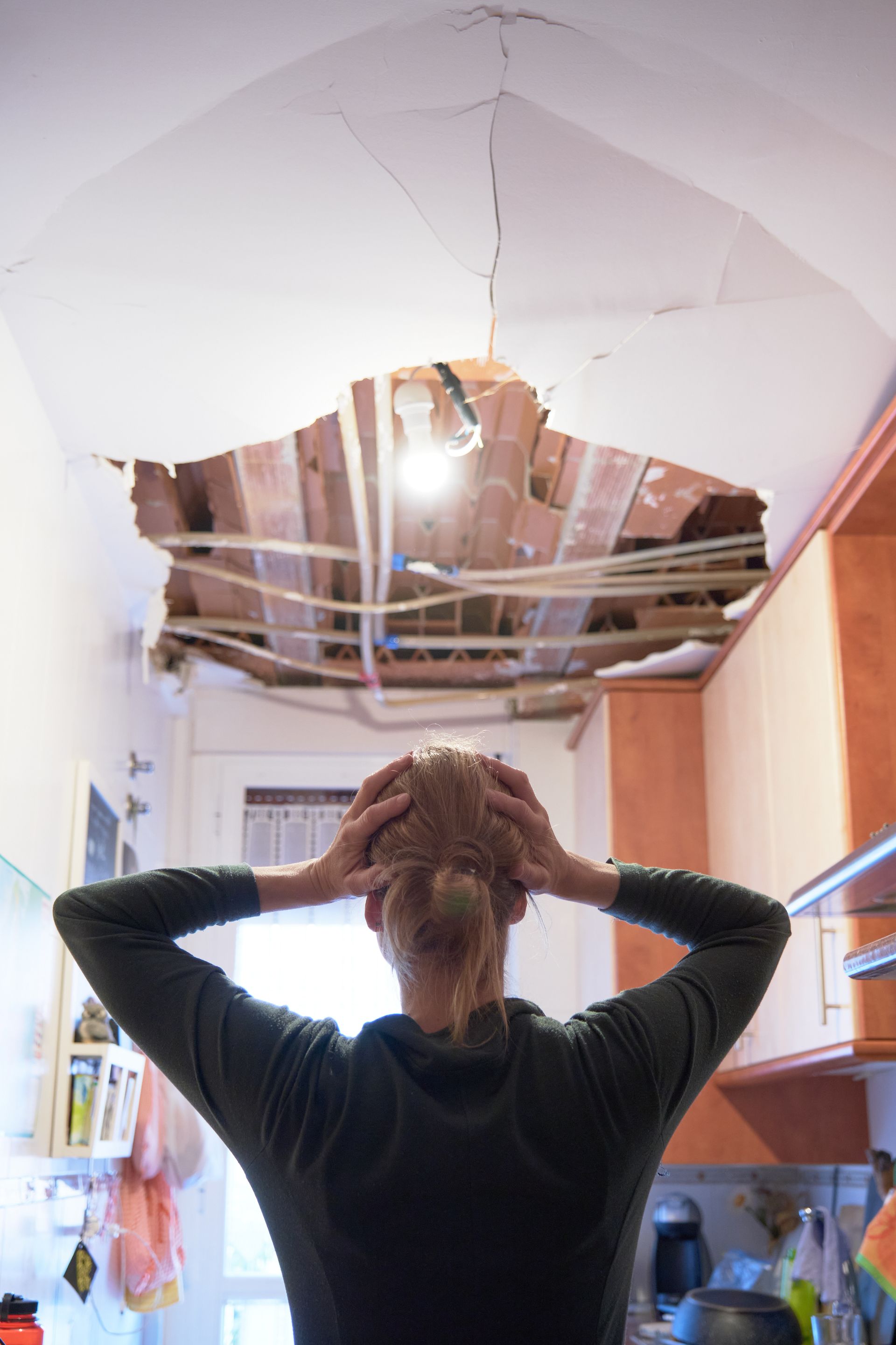 Une femme, les mains sur la tête, regarde le plafond effondré de sa cuisine.