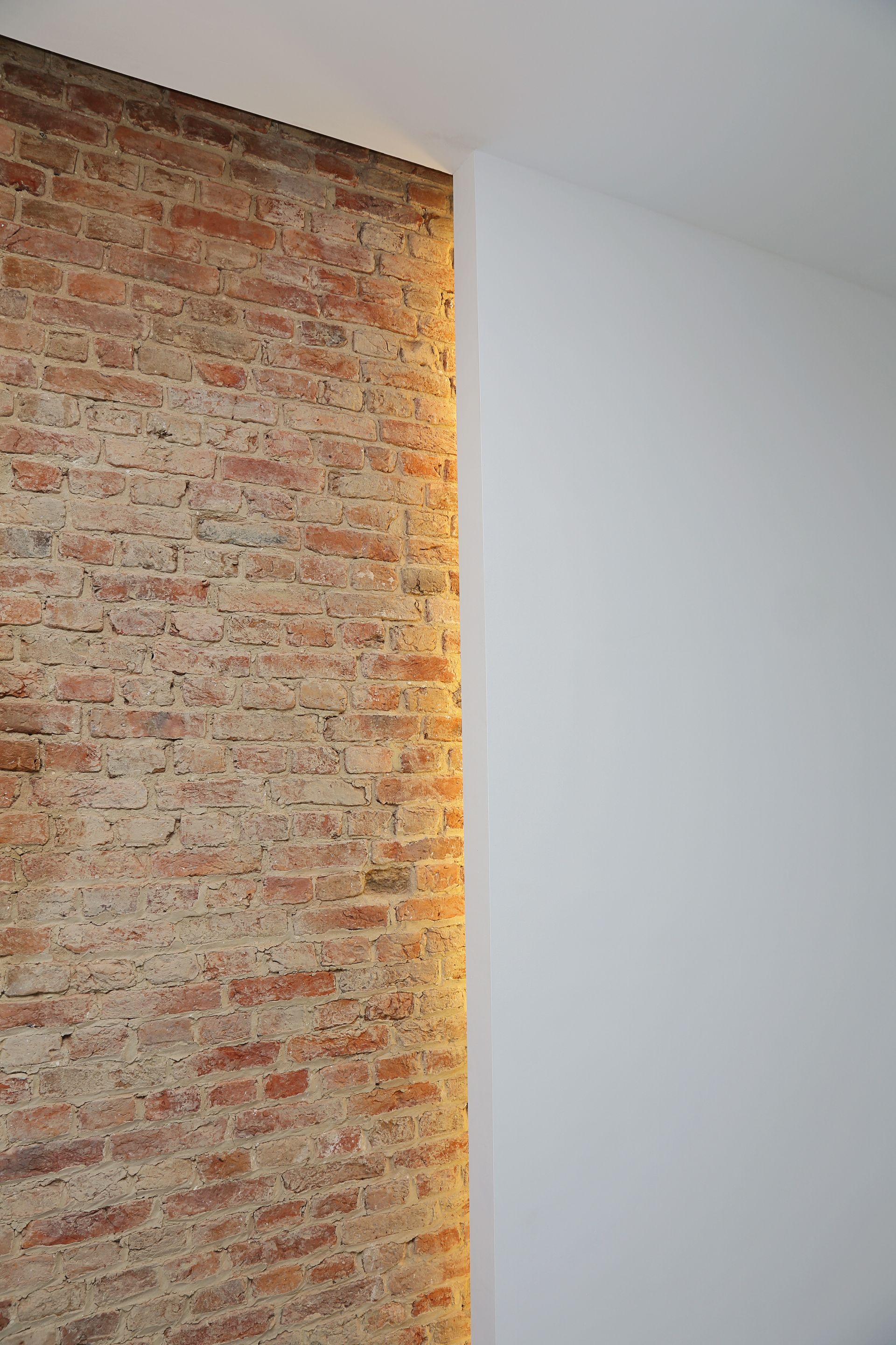 Un mur de briques avec un éclairage chaleureux jouxte un mur blanc lisse.