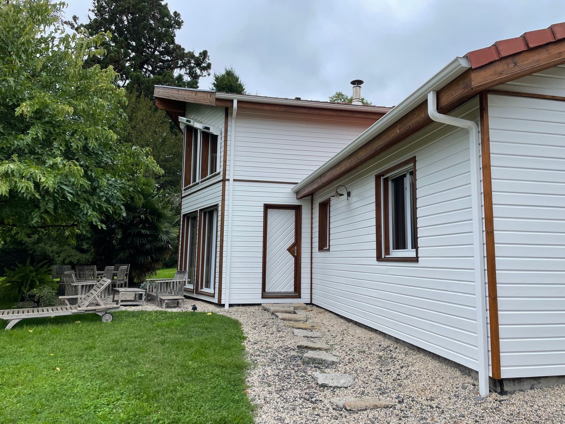 Maison blanche avec des boiseries brunes et un chemin de gravier menant à une porte blanche.
