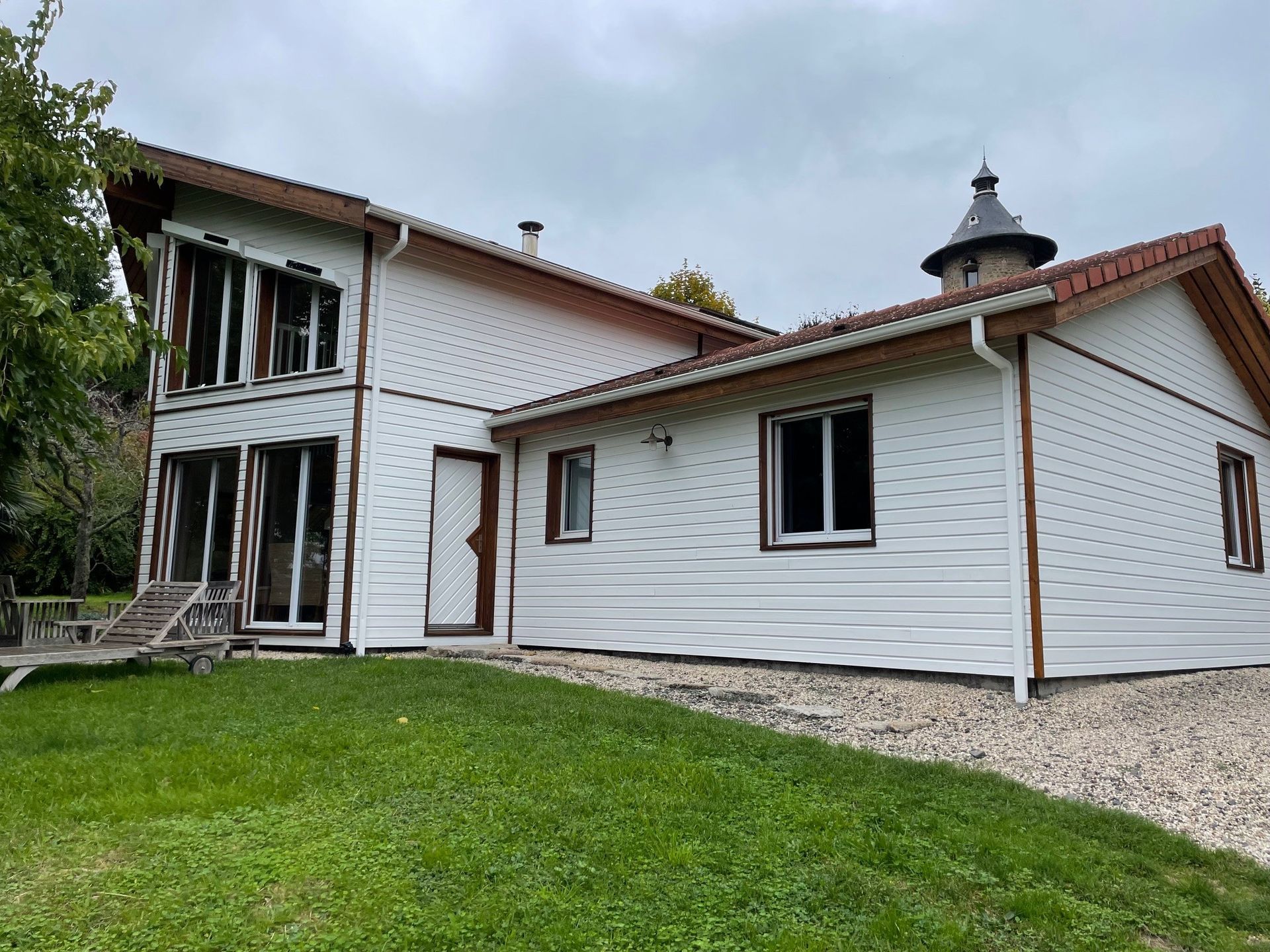 Maison blanche au toit rouge, fenêtres et tour indépendante sur une pelouse verte sous un ciel nuageux.
