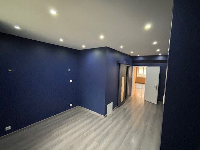 Pièce vide aux murs bleus, au plafond blanc et au sol gris imitation bois. Spots encastrés et deux portes visibles.