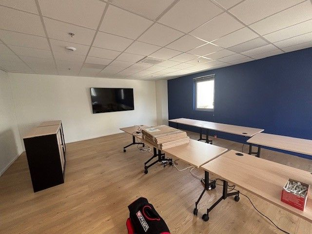 Salle de classe vide avec des bureaux, une télévision et un mur d'accent bleu.
