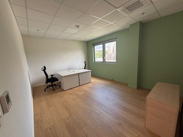 Bureau vide avec bureau, chaise, fenêtre, parquet clair et mur d'accent vert.