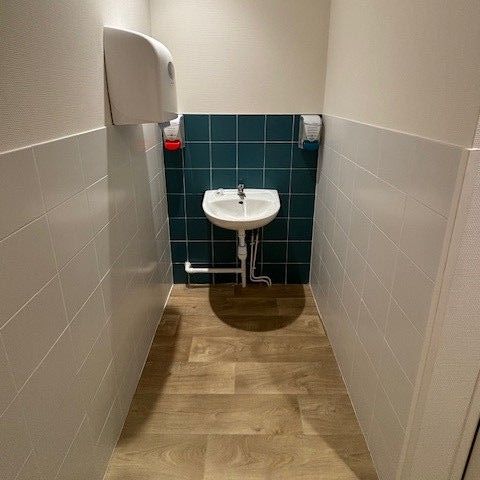Petite salle de bains avec carrelage blanc et turquoise, lavabo, distributeur d'essuie-mains en papier.