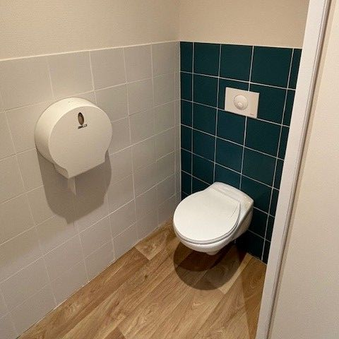 Petite salle de bains avec toilettes et distributeur de papier essuie-mains.