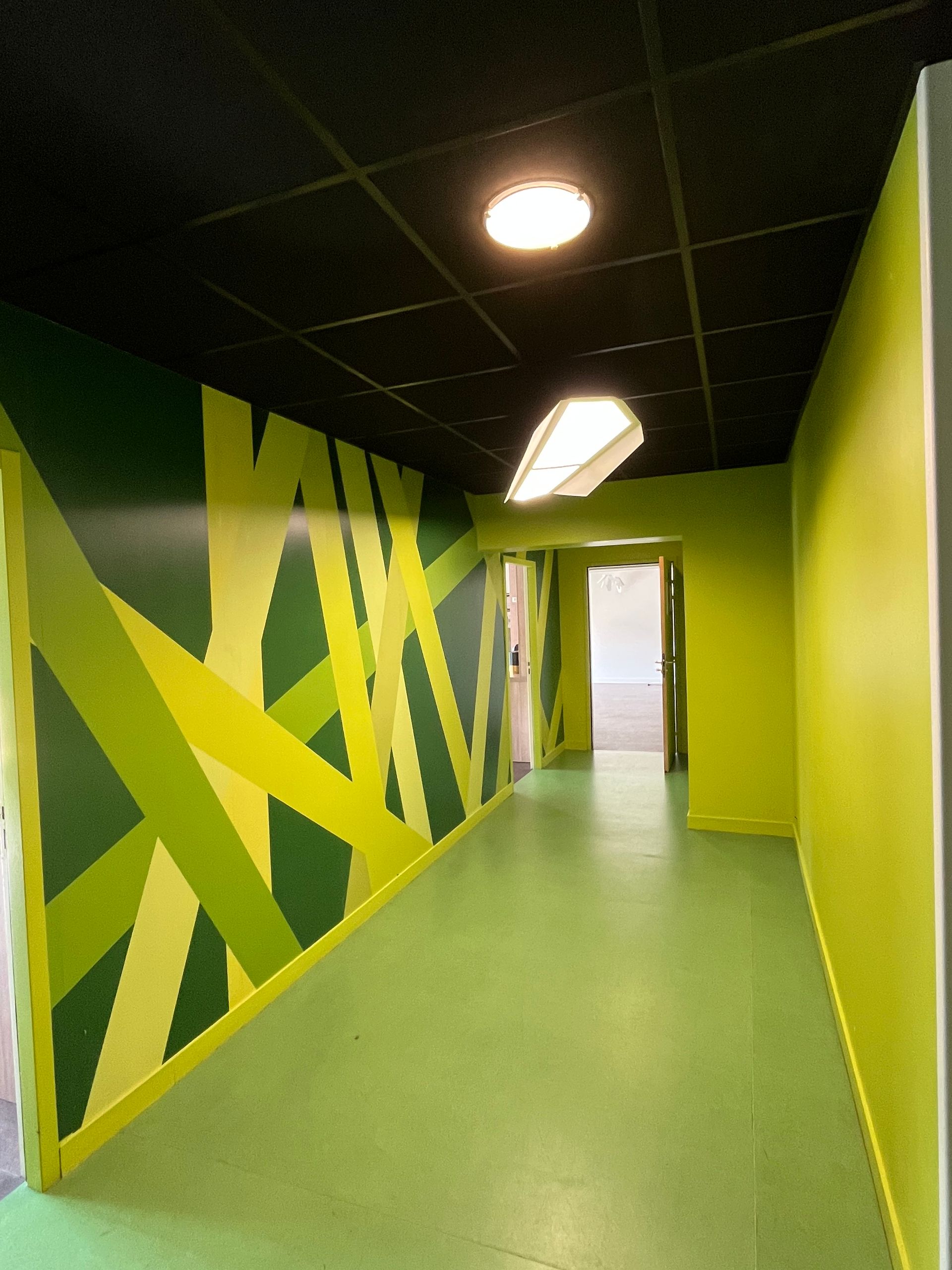 Un couloir étroit aux murs et au sol verts. Un mur est orné de motifs géométriques vert clair et vert foncé.